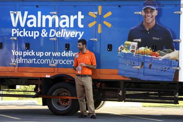 A Walmart Pickup-Grocery employee waits next to a truck.